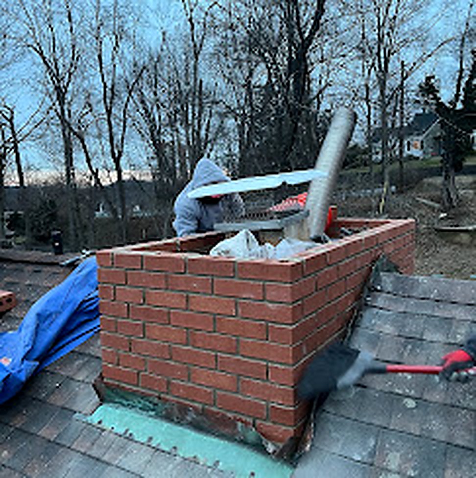 Worker mid-rebuild on brick chimney, drone view